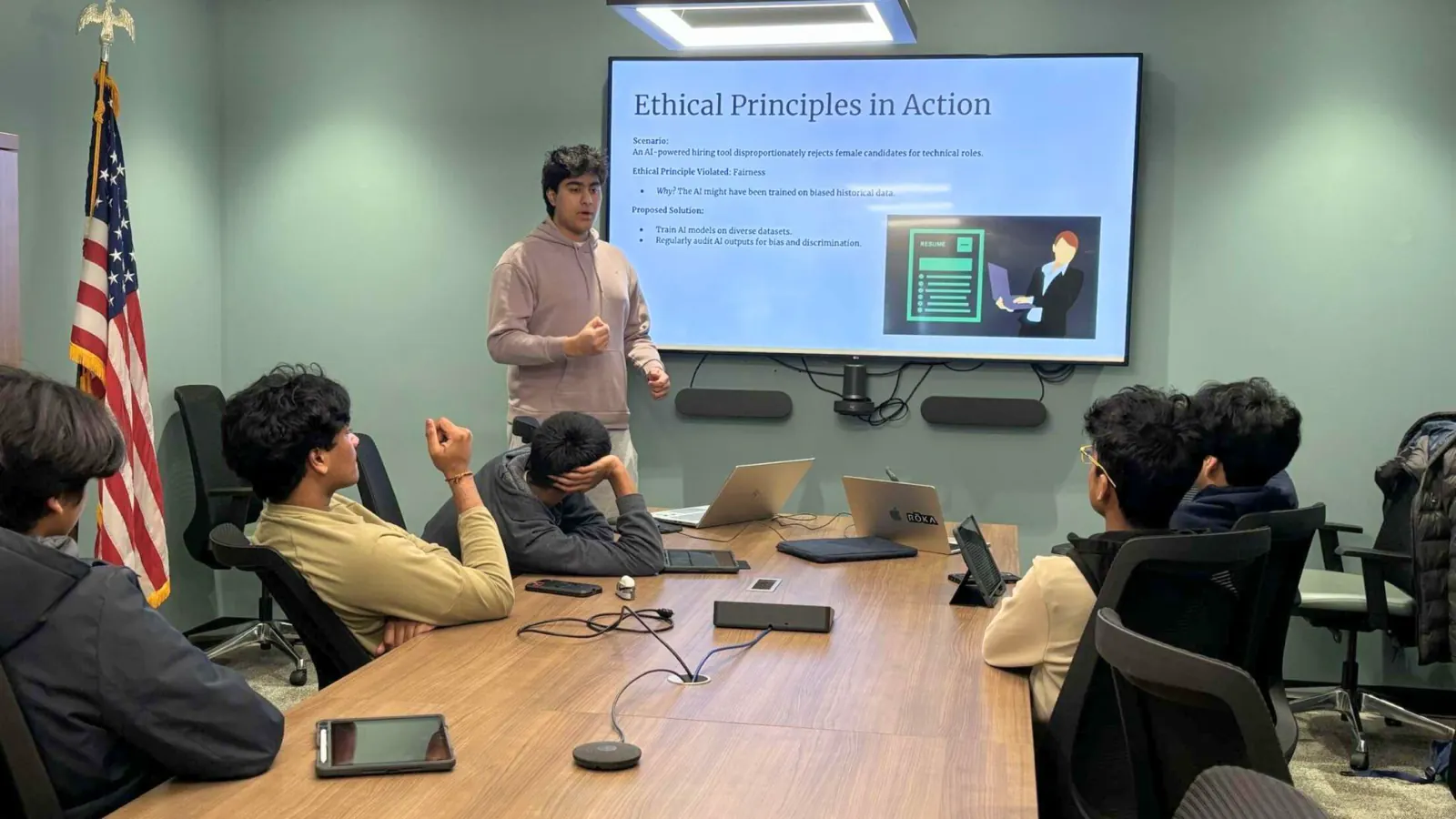 A student presents a slide titled “Ethical Principles in Action” to peers around a conference table.